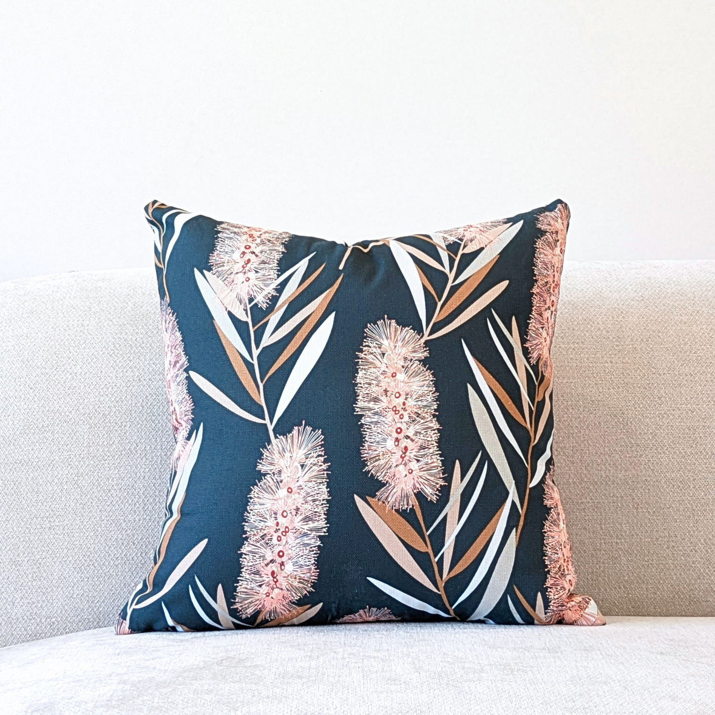 The Emotive Collection Bottlebrush Cushion Cover is a square cotton canvas cover with a dark background and Jocelyn Proust-inspired botanical design, featuring pale pink and tan bottlebrush flowers with green leaves.