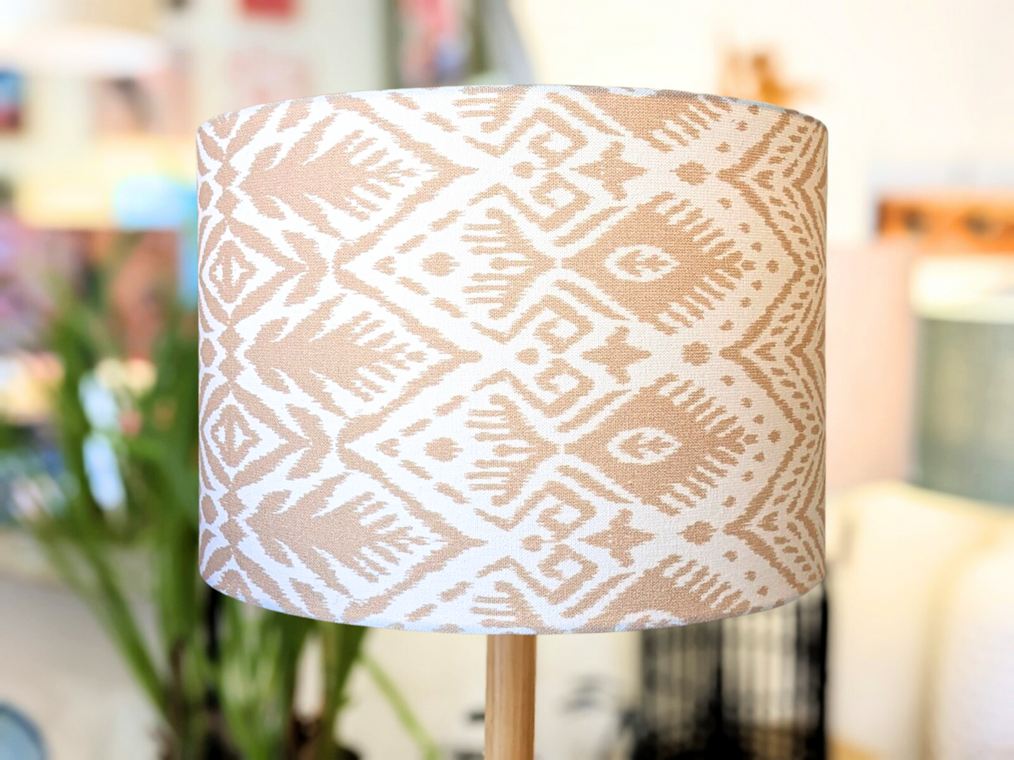 A close-up of the Emotive Collection’s Ikat Lampshade, showcasing beige and white geometric diamond patterns, set against a softly blurred indoor background. Discover unique sizes in this handcrafted design.