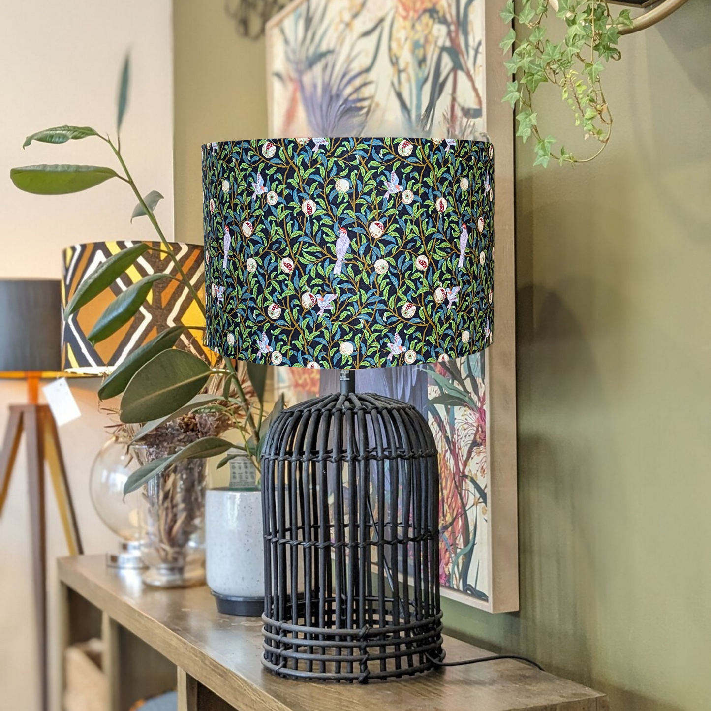 Handmade Bird & Pomegranate Black William Morris lampshade by Emotive Collection, shown on a Black rattan lamp base, featuring a striking black background with vibrant bird and pomegranate motifs in the classic Morris style. Crafted with precision in Aust