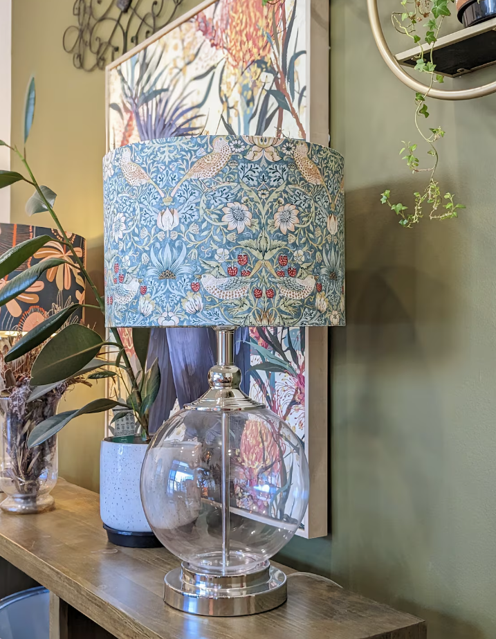 Handmade William Morris Strawberry Thief lampshade by Emotive Collection on a glass lamp base, featuring the iconic design with intricate floral motifs on a soft aqua blue background. Expertly crafted in Australia, this timeless piece enhances your home w