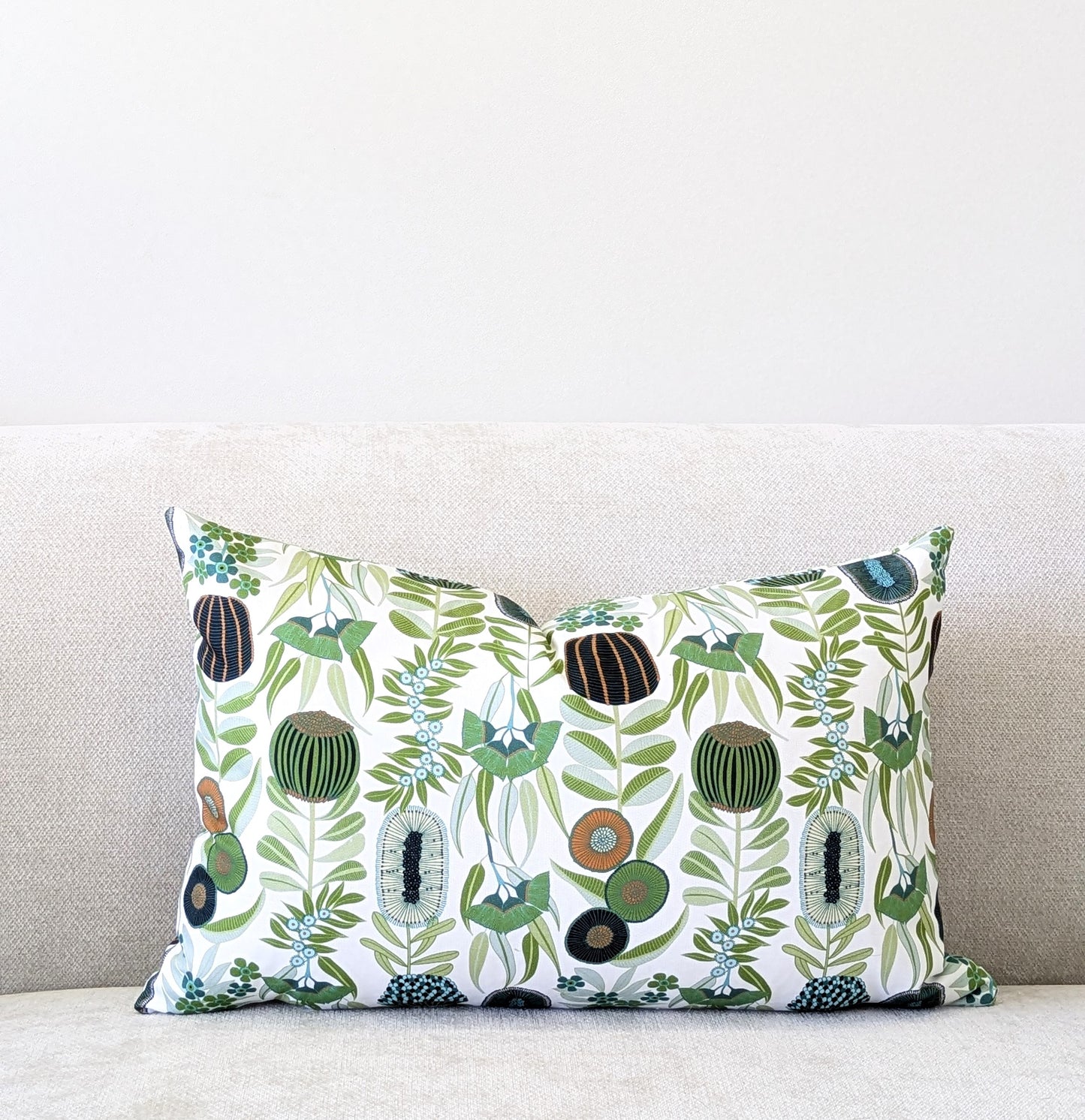 The Green Australiana Cushion Cover by Emotive Collection, featuring a design by Jocelyn Proust on cotton canvas, sits on a light beige sofa against a pale wall.