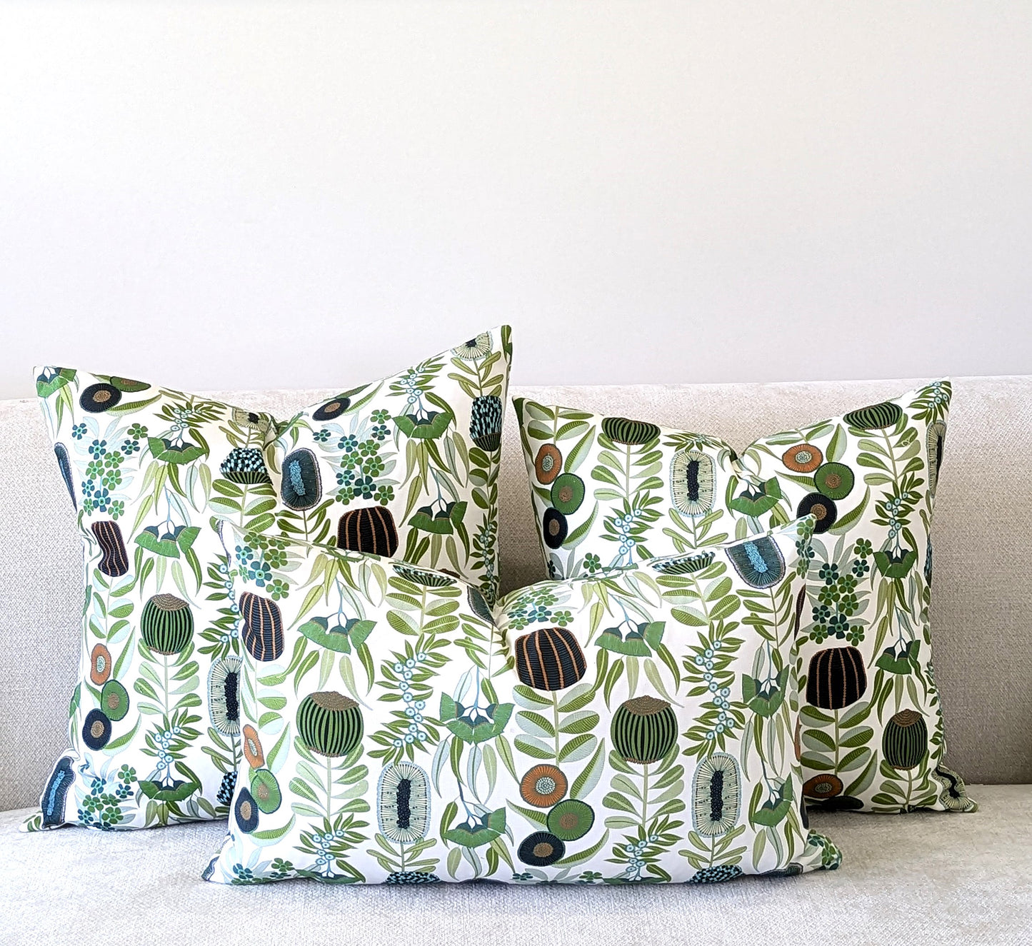 Three Green Australiana Cushion Covers from Emotive Collection, crafted from cotton canvas and designed by Jocelyn Proust, are arranged on a light-colored sofa against a plain white wall.