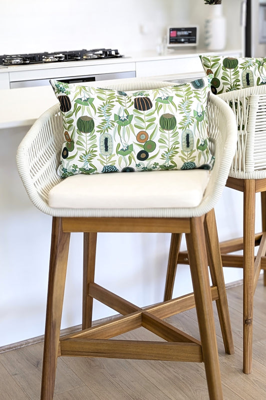 A white and wood bar stool with a cushioned seat features the Emotive Collections Green Australiana Cushion Cover, adding a modern touch beside the kitchen’s white counter and stove.