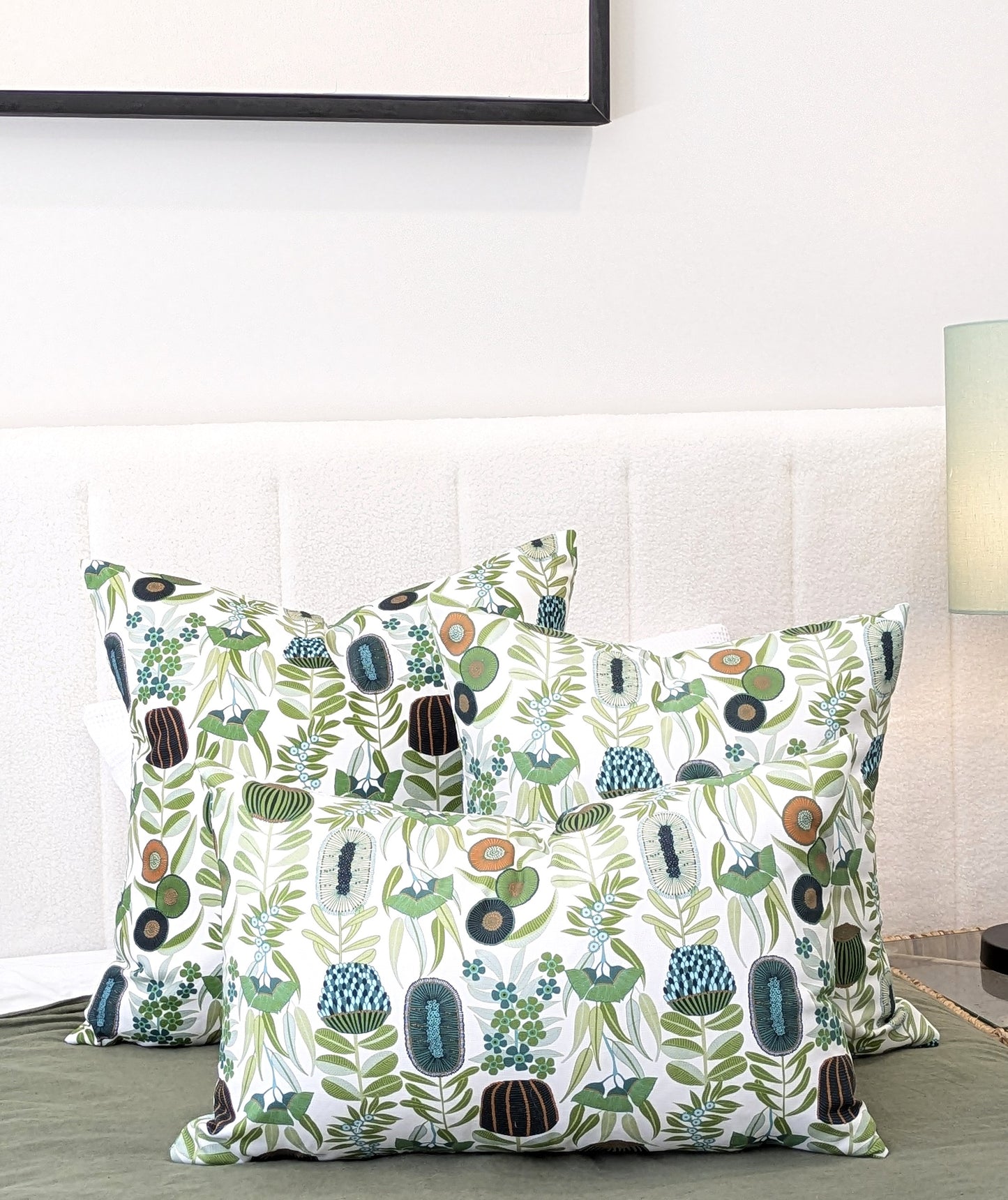 Three Green Australiana Cushion Covers by Emotive Collection are displayed on a bed with a white padded headboard, paired with a green bedspread and a green lamp for a fresh, botanical style.
