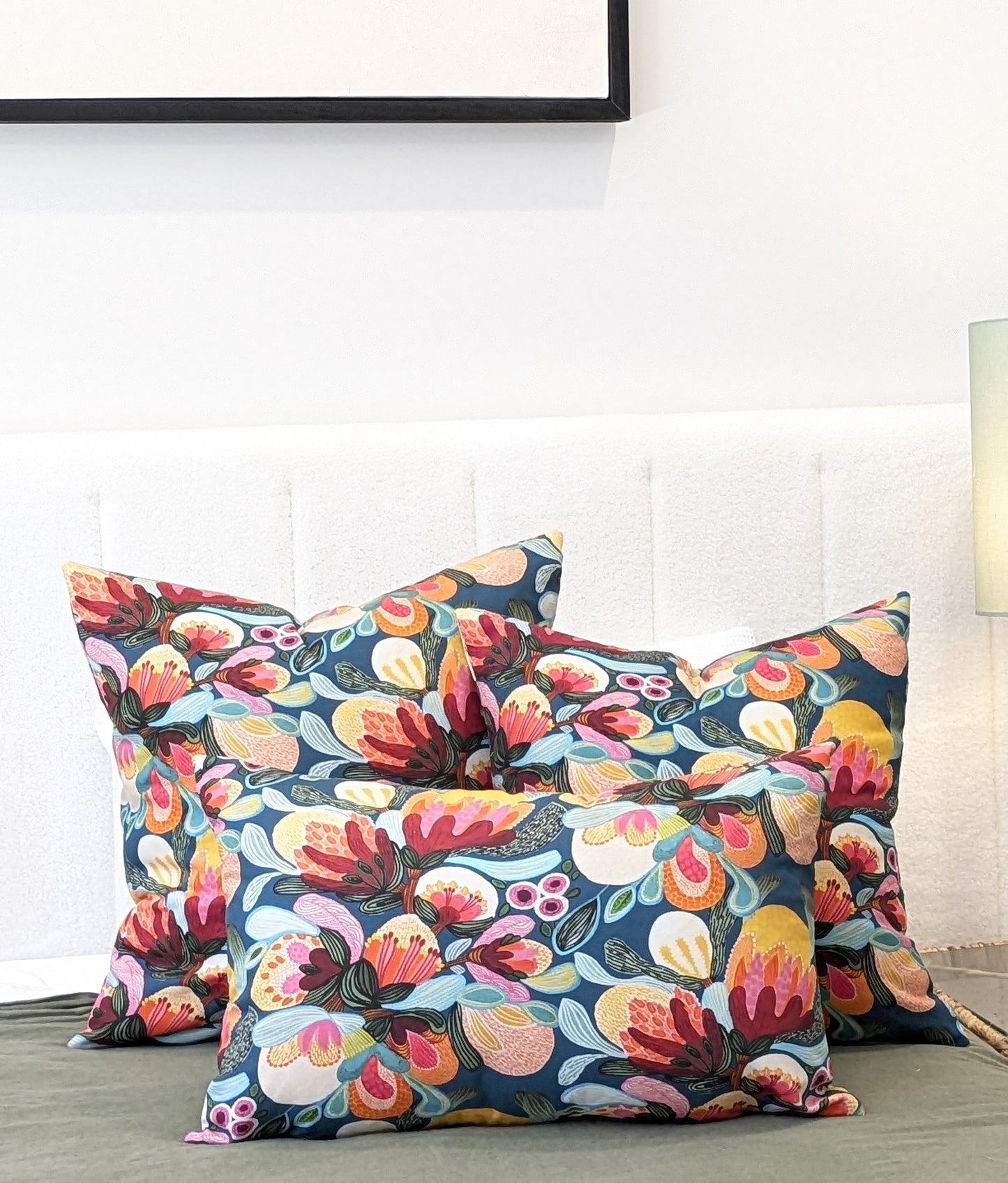 Three decorative pillows, including the Emotive Collections Midnight Bush Cushion Cover, are arranged on a green surface before a white upholstered headboard, with a lamp and part of a framed picture visible in the background.
