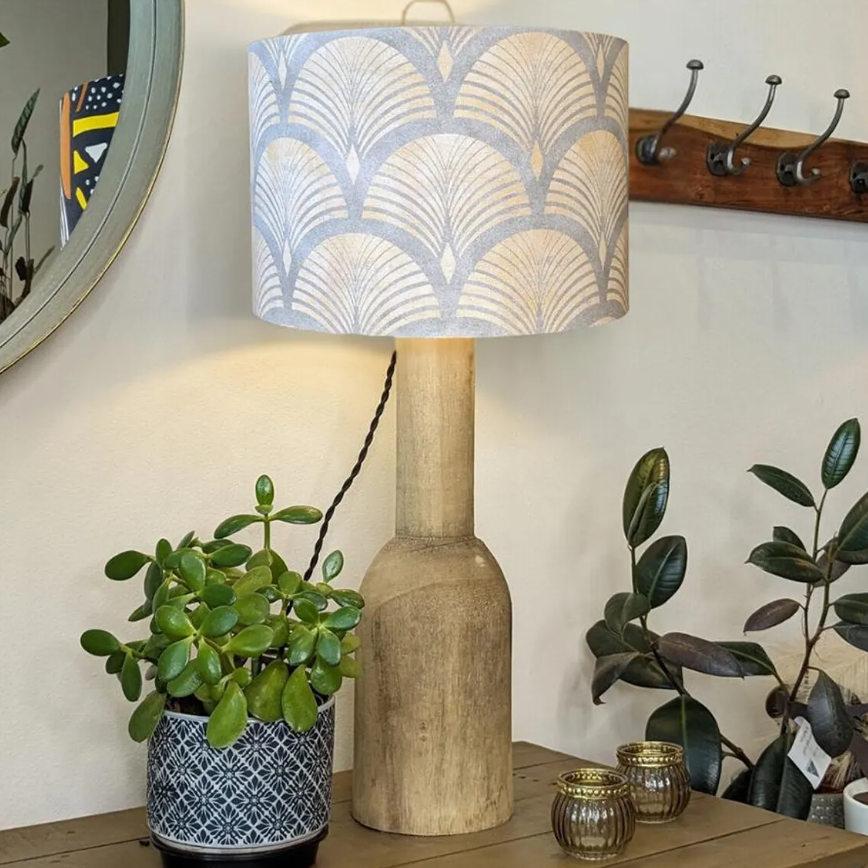 An Emotive Collection Art Deco Lampshade atop a handcrafted wooden table lamp stands beside a potted plant. A wall mirror, coat rack, and decorative jars in the background evoke cozy South Australia charm.