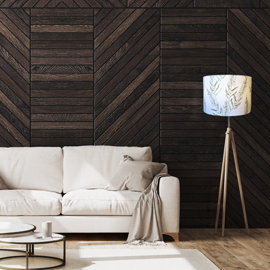 A modern living room features a beige linen-blend sofa with pillows, a gray throw, and a dark chevron wood wall. On the right stands an Emotive Collection Bottlebrush Green Lampshade floor lamp, with two round coffee tables in front.