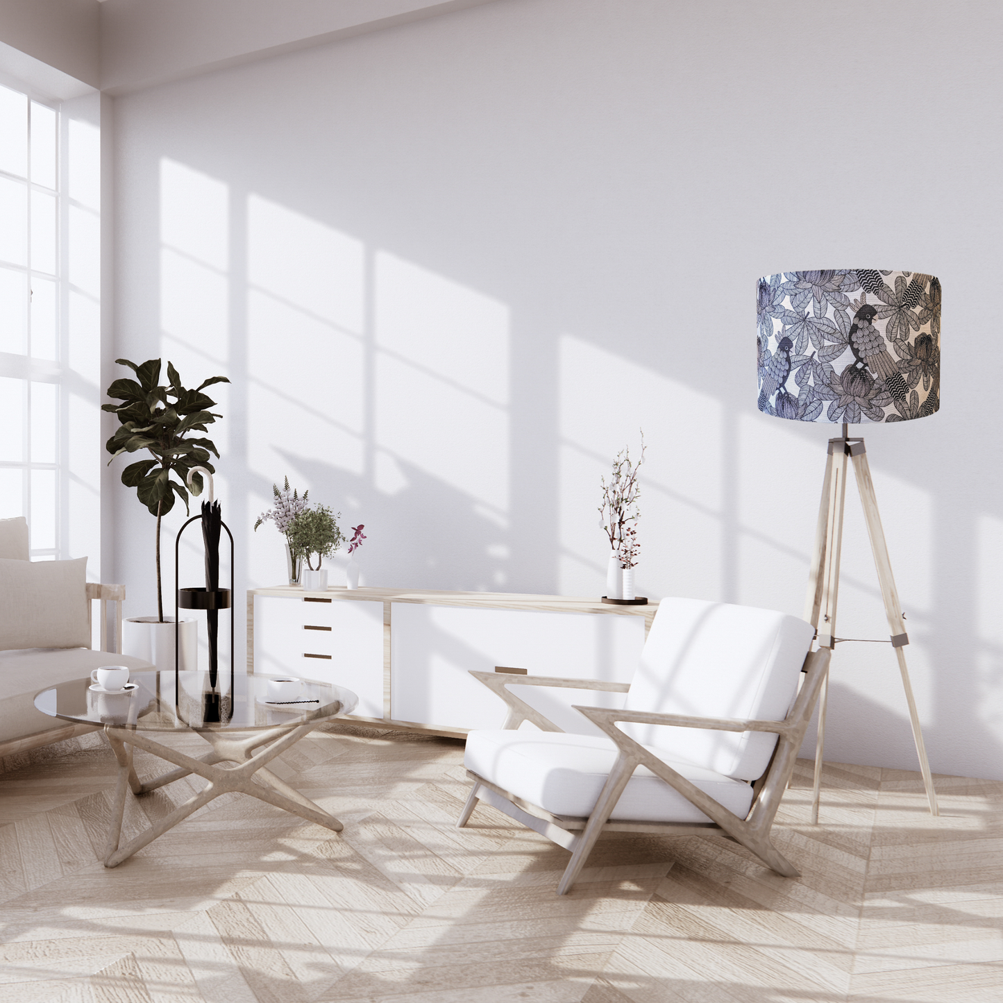 Bright, modern living room with a white armchair, glass coffee table, potted plants, abstract prints, white sideboard, and a standing lamp featuring the Australian Cockatoo Lampshade by Emotive Collection. Sunlight streams through large windows onto the light wooden floor.