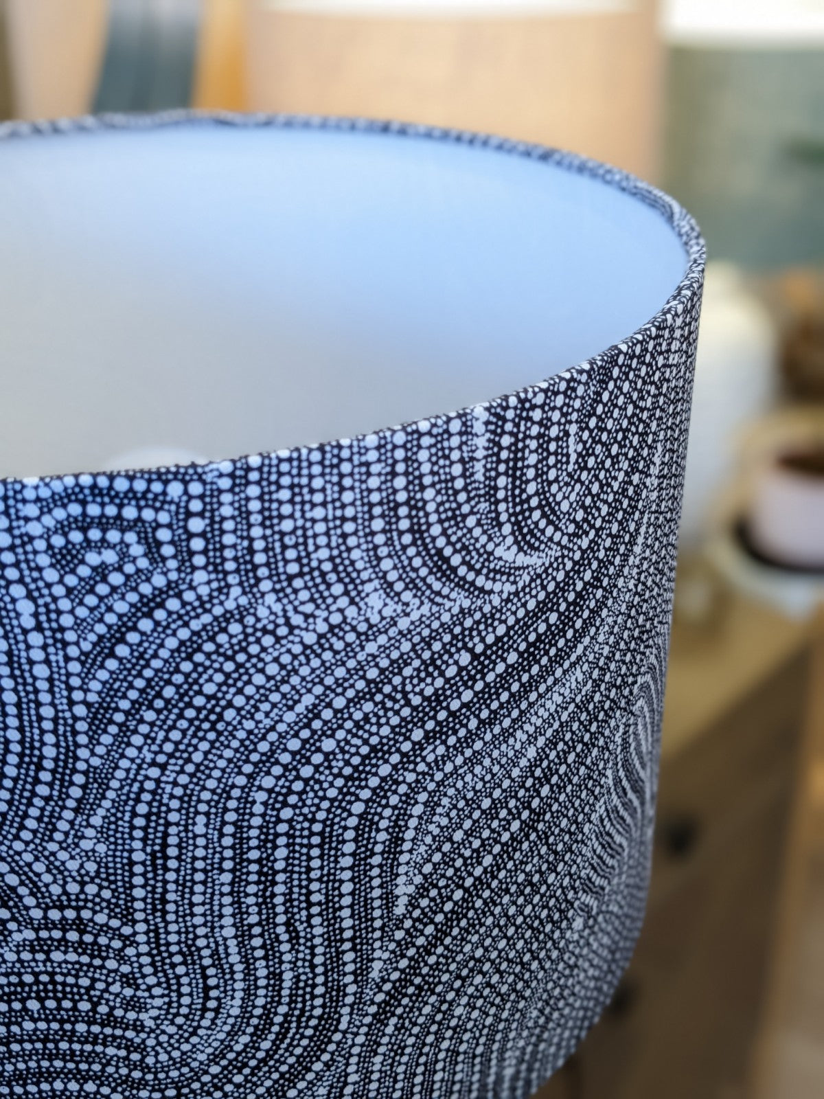 Close-up of the Desert Dreaming Aboriginal lampshade by artist Senita Napangardi Granites, featuring a black-and-white dotted wavy pattern inspired by Desert Fringe-Rush Seed Dreaming. Softly blurred background shows hints of furniture.