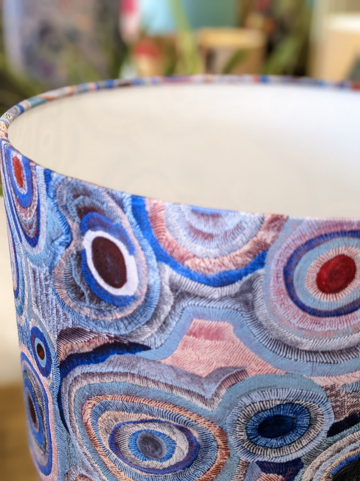 A close-up of the Aboriginal Water Dreaming Pastel Lampshade by artist Senita Napangardi Granites, featuring colorful embroidered patterns inspired by Desert Fringe-Rush Seed Dreaming (Lukarrara Jukurrpa), with a blurred background.
