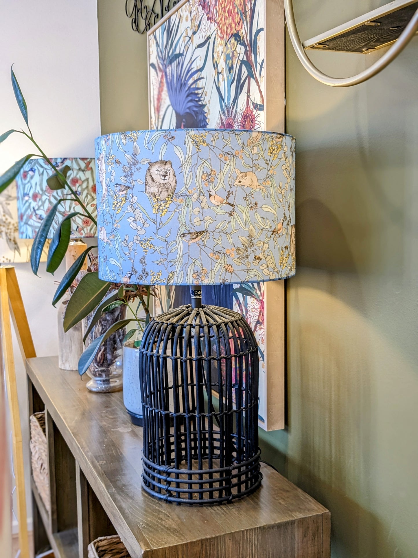The Wombat & Wattle lampshade is shown here on a black rattan lamp base, showcasing a whimsical design by Australian artist Victoria McGrane from The Scenic Route. Handcrafted in Australia with care and attention to detail.
