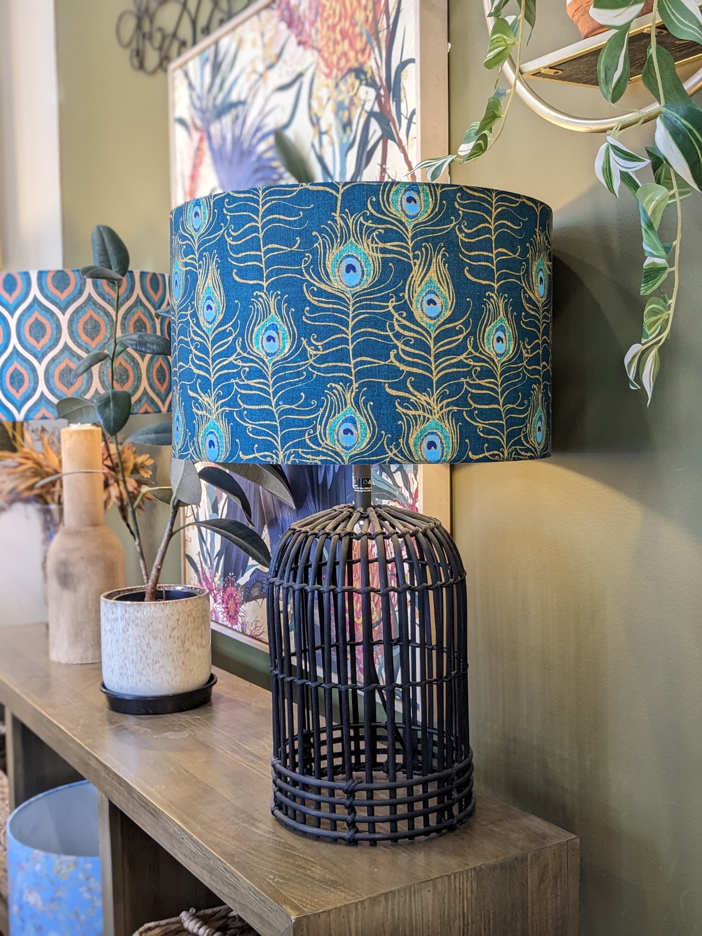 Peacock Feather Nouveau lampshade on a Black Rattan lamp base, featuring luxurious gold-toned peacock feathers on a rich blue background. Designed by Australian artist Cecilia Mok and crafted in Australia for a touch of elegance.