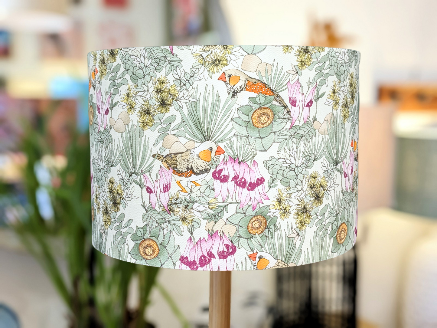 The Zebra Finches Lampshade (35cm x 24cm) by Victoria McGrane - The Scenic Route features hand-illustrated birds, green leaves, and pink flowers, bringing Australiana charm to your decor. Only 2 available.