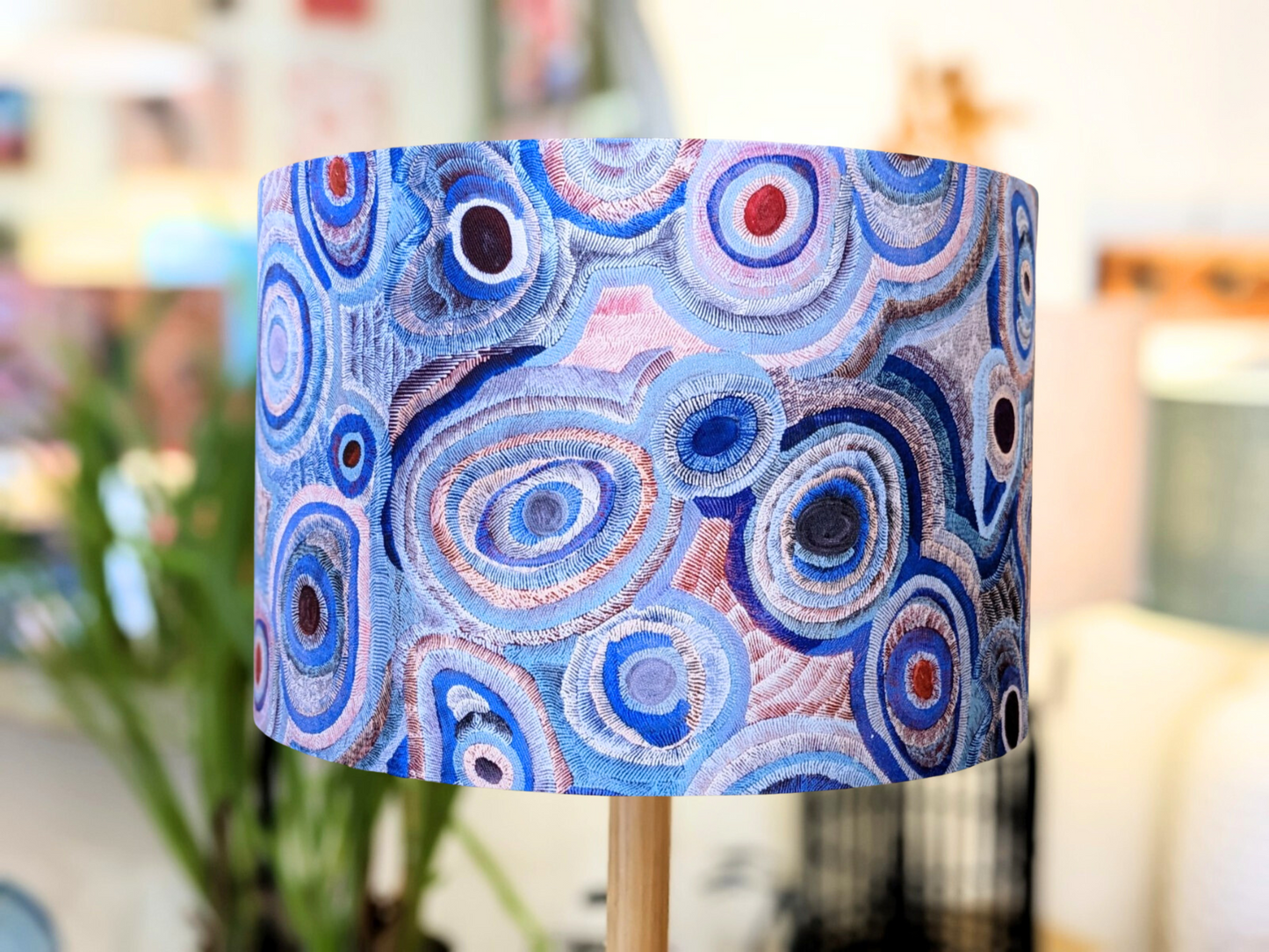 The Aboriginal Water Dreaming Pastel Lampshade by artist Senita Napangardi Granites features an abstract pattern of blue, purple, and pink concentric circles on a softly blurred background, inspired by Desert Fringe-Rush Seed Dreaming.