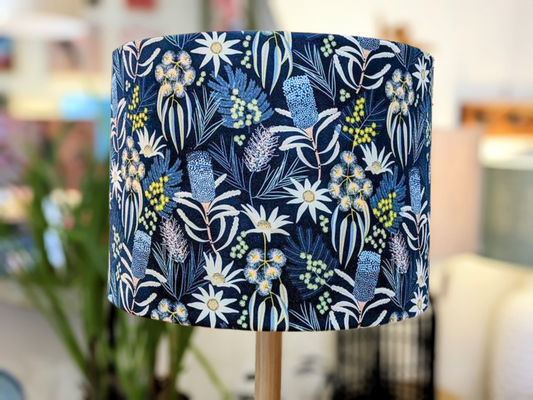 The Blue Native Floral Lampshade from the Emotive Collection features a vibrant botanical design on a navy background, handmade in a cylindrical shape and mounted on a wooden stand, designed by Australian artist Jocelyn Proust.
