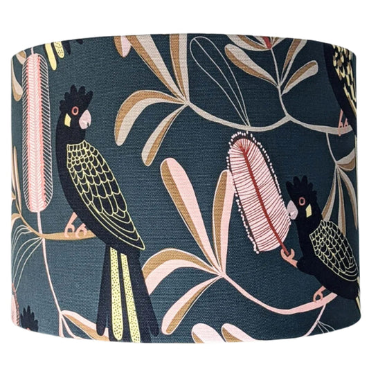 The Emotive Collection’s Yellow-Tailed Black Cockatoo Lampshade features a dark background with Jocelyn Proust botanical patterns of pale pink and tan leaves and stylized birds from the Australian Flora Collection.