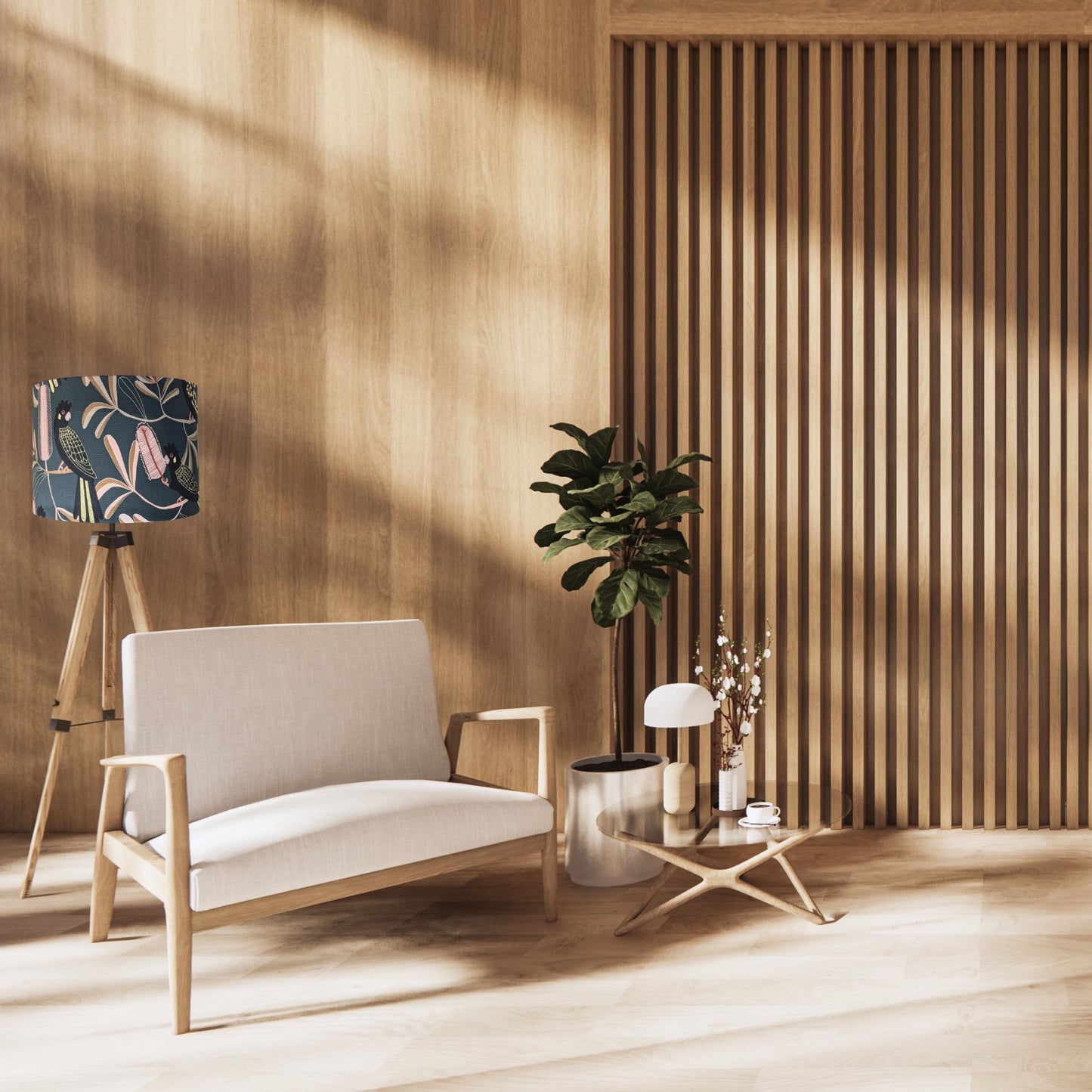 A modern, minimalist living room with light wood walls and floor, a beige two-seater sofa, a small round table with decor, and a tripod lamp featuring the Emotive Collection Yellow-Tailed Black Cockatoo Lampshade. Sunlight streams in by the leafy potted plant.