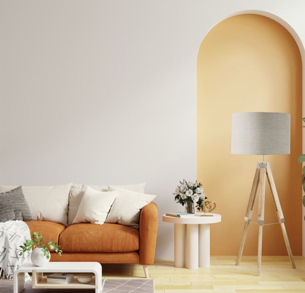 A modern living room with a tan sofa, neutral pillows, a white side table with flowers, and a tall tripod floor lamp featuring the Emotive Collections Stone Premium Linen Lampshade. An arched yellow accent wall and plants add an earthy touch.