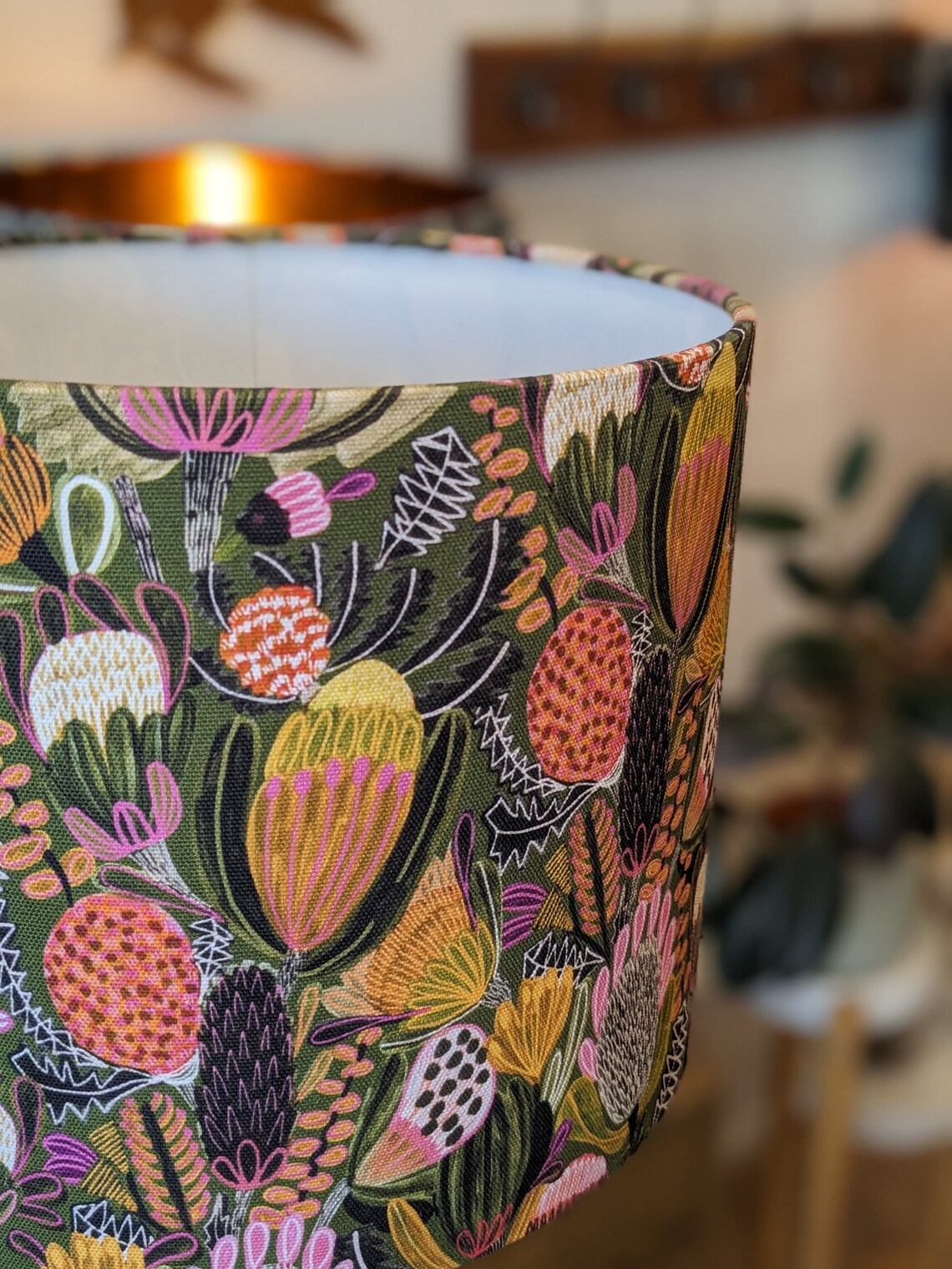 Close up of Handmade Bush Banksia lampshade by Emotive Collection, showcasing colorful Banksia blooms on a green backdrop. Designed by Australian artist Jocelyn Proust and made with love in Australia.