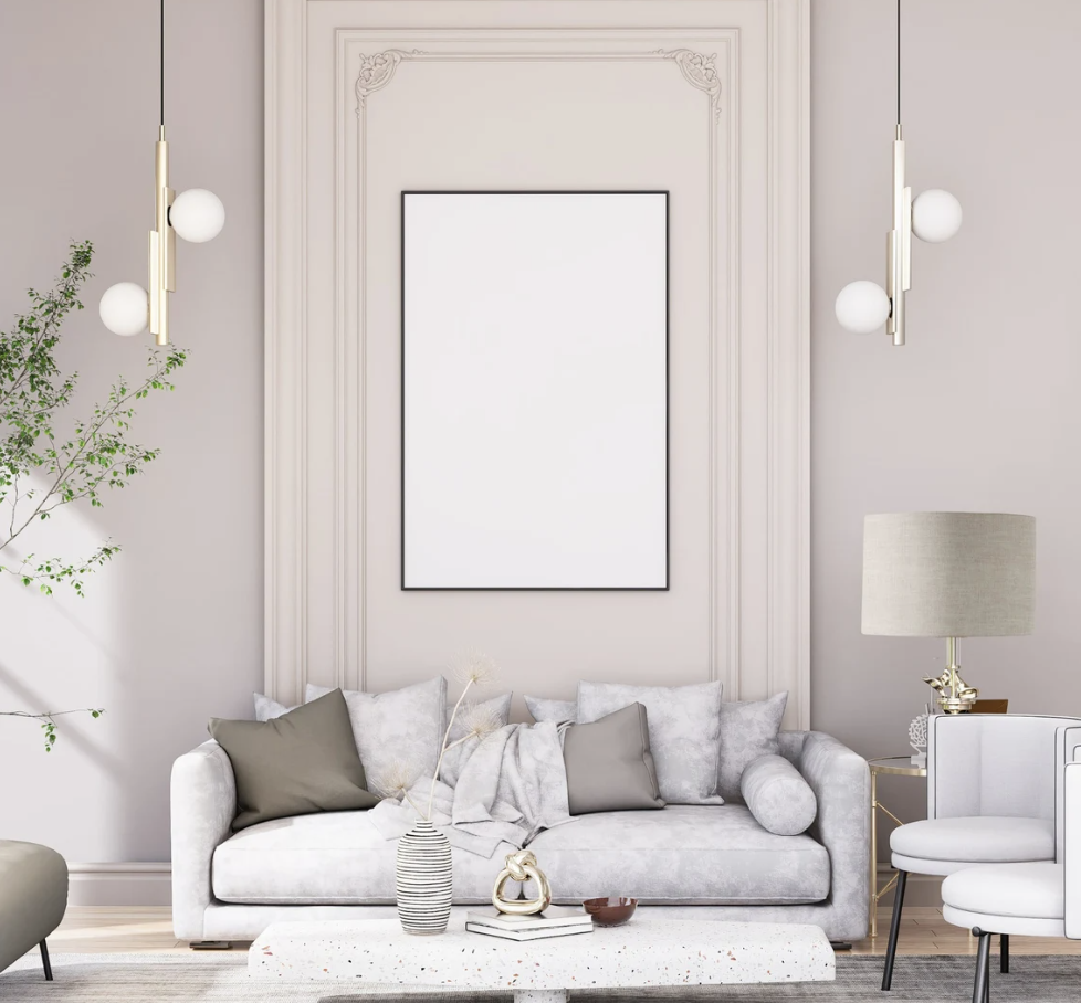 A modern living room with a white sofa, gray and beige pillows, blank wall art, pendant lights, a tall plant, and a side table showcasing the Emotive Collection’s Stone Premium Linen Lampshade alongside decorative vases.