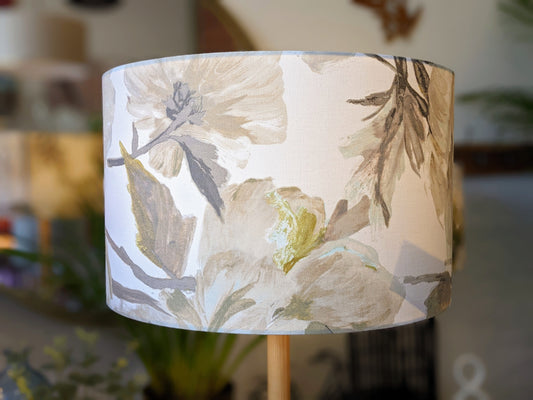 A close-up of the In Bloom Lampshade by Emotive Collection, featuring a handmade floral design in muted pastel beige, green, and gray tones, set against a softly blurred background.