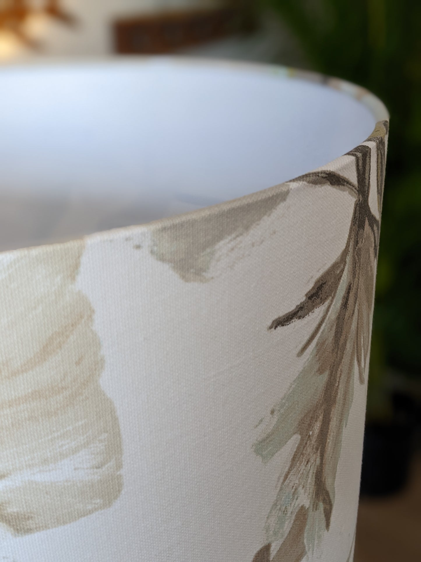 Close-up of the In Bloom Lampshade from the Emotive Collection, showcasing a soft beige and light green floral pattern on a handmade shade, set against a blurred background with hints of greenery.
