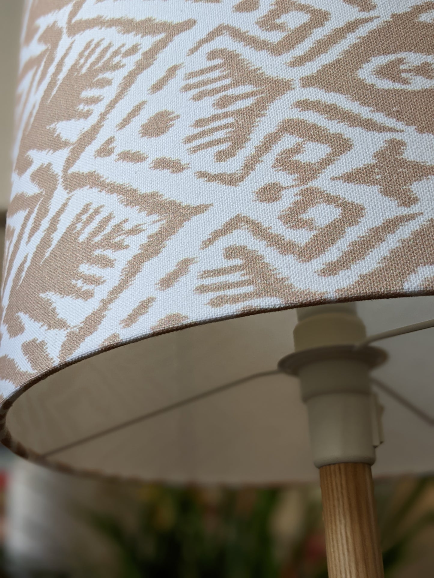 Close-up of the Ikat Lampshade from the Emotive Collection, showcasing a beige and white geometric fabric pattern. Displayed on a wooden stand, this design is available in multiple sizes against a softly blurred background.