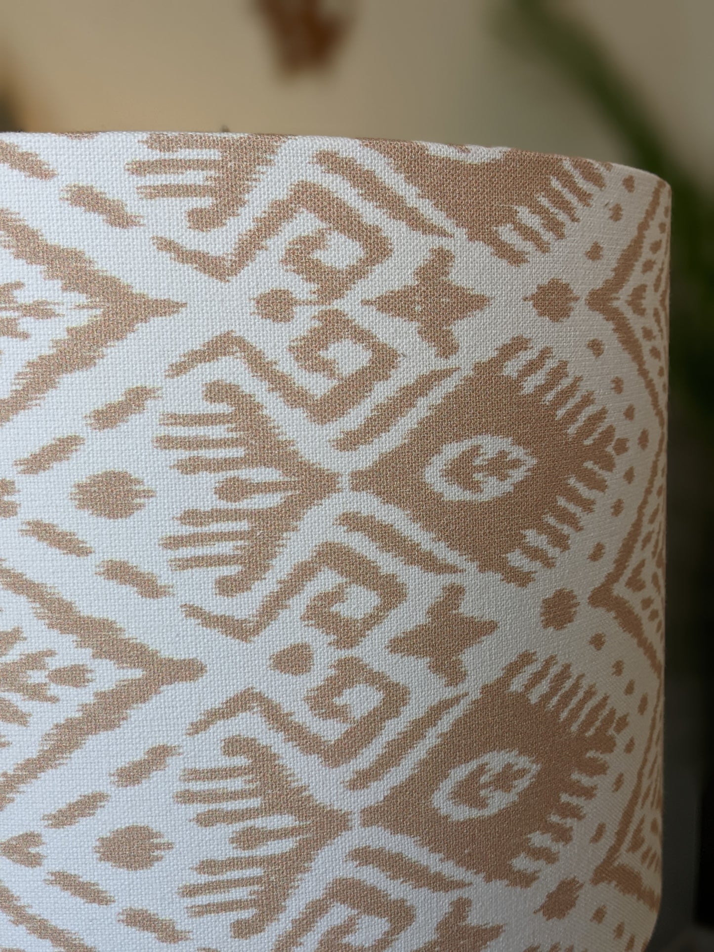 A close-up of the Ikat Lampshade by Emotive Collection, featuring beige and white geometric and tribal patterns with diamonds, lines, and abstract shapes. The background is softly blurred.