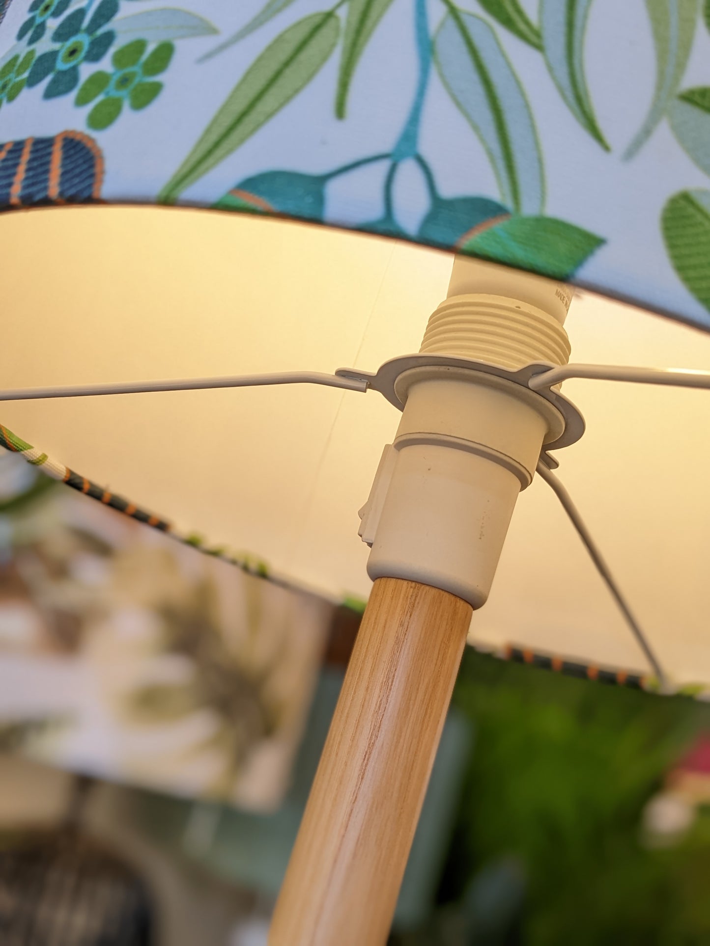 Close-up of an Emotive Collection lamp with a wooden stem and Green Australiana Lampshade, featuring vibrant green and blue leafy patterns. The photo highlights the connection between the base and the shade.