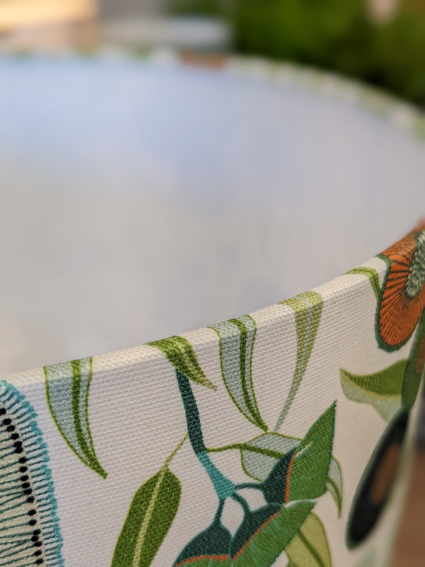 A close-up of the Green Australiana Lampshade by Emotive Collection, featuring a fabric with green leaves and orange flowers, inspired by Jocelyn Proust and proudly Australian Made, set against a softly blurred background.
