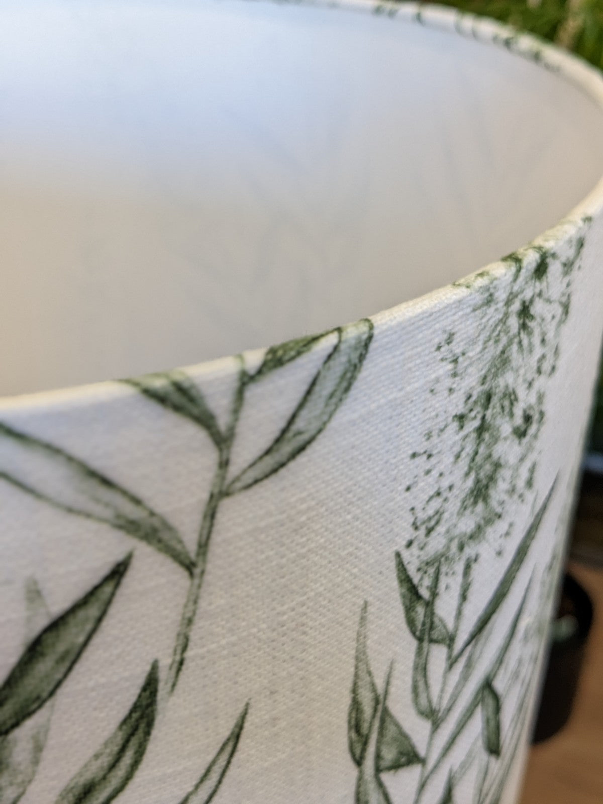 Close-up of the Bottlebrush Green Lampshade from the Emotive Collection, showcasing its subtle green botanical leaf pattern on linen blend fabric with a textured surface and intricate design details.