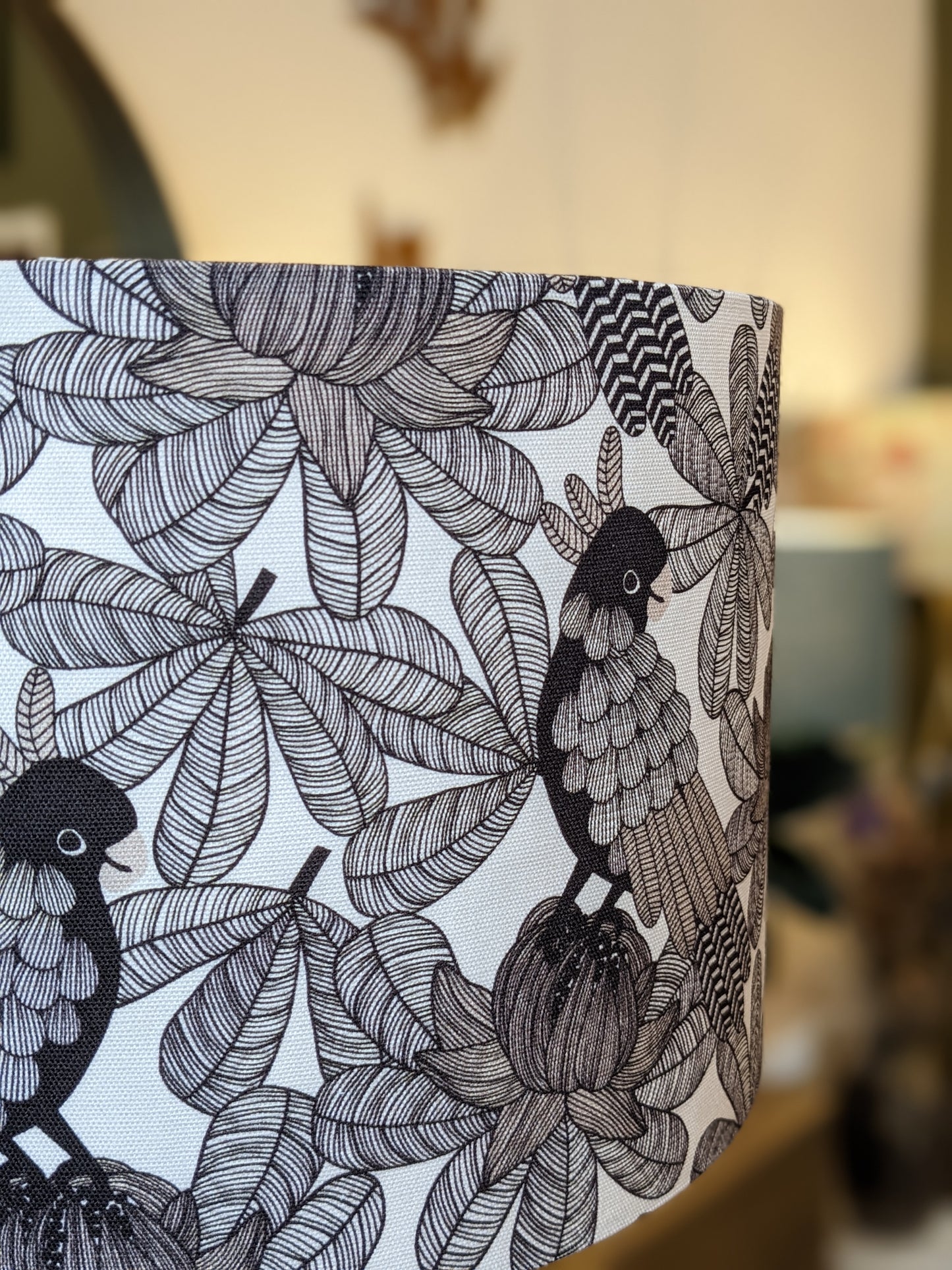 The Australian Cockatoo Lampshade by Emotive Collection features a detailed black-and-white bird pattern on handmade fabric, with perched cockatoos among stylized leaves and flowers, set against a softly blurred background.