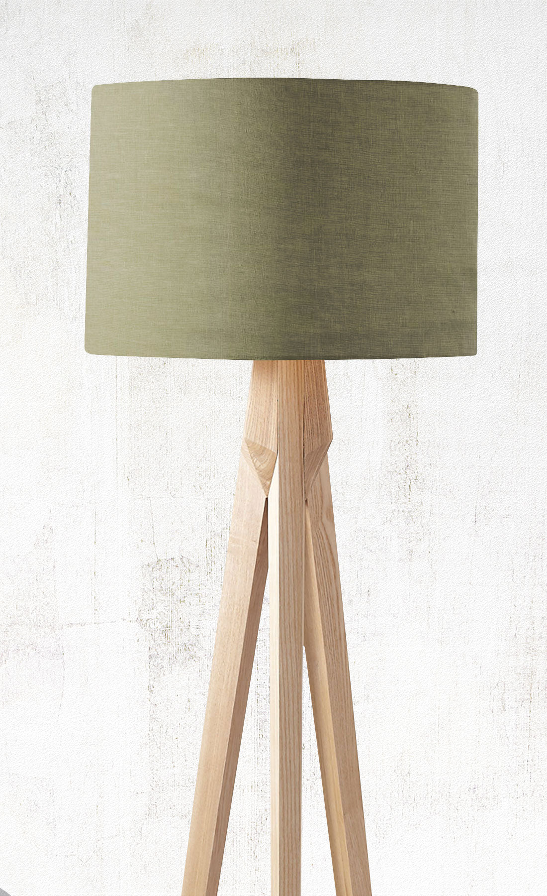 The Emotive Collection’s Sage Premium Linen Lampshade sits atop a modern tripod floor lamp with a light wooden base, beautifully set against a textured off-white wall.