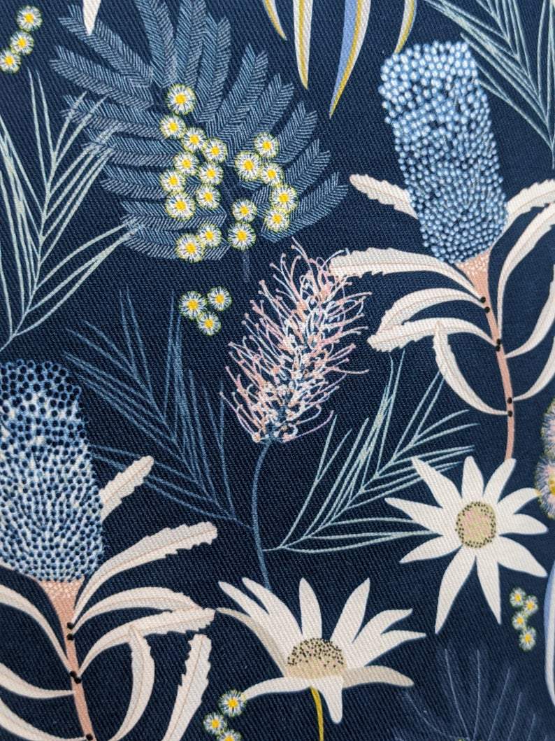 The Blue Native Floral Lampshade from Emotive Collection features a dark blue base with a botanical design of white and yellow flowers, blue flower spikes, and green leaves, created by Australian designer Jocelyn Proust.