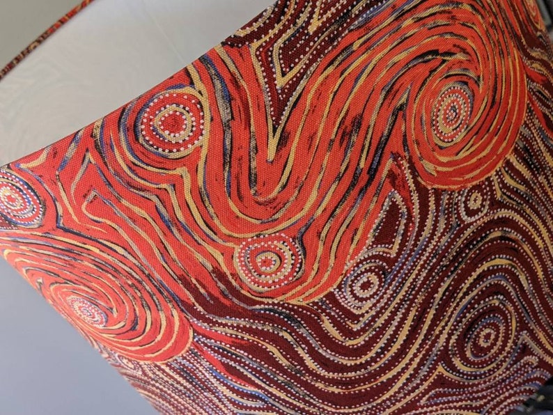 The Indigenous Aboriginal Warlu Mina Mina Dreaming Lampshade by artist Pauline Napangardi Gallagher features vibrant, abstract red, orange, yellow, and white patterns on a neutral background, inspired by traditional Aboriginal art.