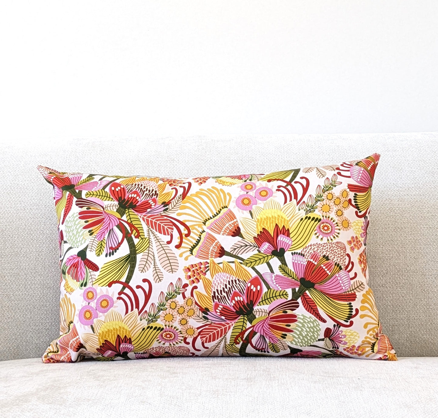 The Emotive Collection Wild Protea Cushion Cover features vibrant floral cotton canvas and adorns a light cream sofa set against a plain white wall.