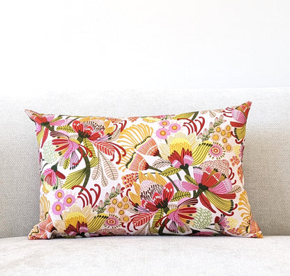 The Emotive Collection Wild Protea Cushion Cover features vibrant floral cotton canvas and adorns a light cream sofa set against a plain white wall.