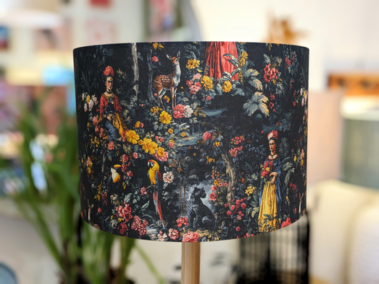 The Frida Kahlo Lampshade by Emotive Collection features a vibrant, detailed pattern of people, animals, parrots, a deer, and tropical foliage on a dark background—a striking Australian-made accent for your space.