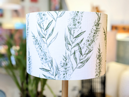 A close-up of the Bottlebrush Green Lampshade from the Emotive Collection, handmade in a linen blend with a green leafy botanical pattern on white, set against a softly blurred indoor background.