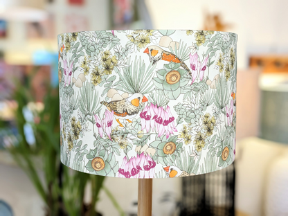 The Zebra Finches Lampshade (35cm x 24cm) by Victoria McGrane - The Scenic Route features hand-illustrated birds, green leaves, and pink flowers, bringing Australiana charm to your decor. Only 2 available.