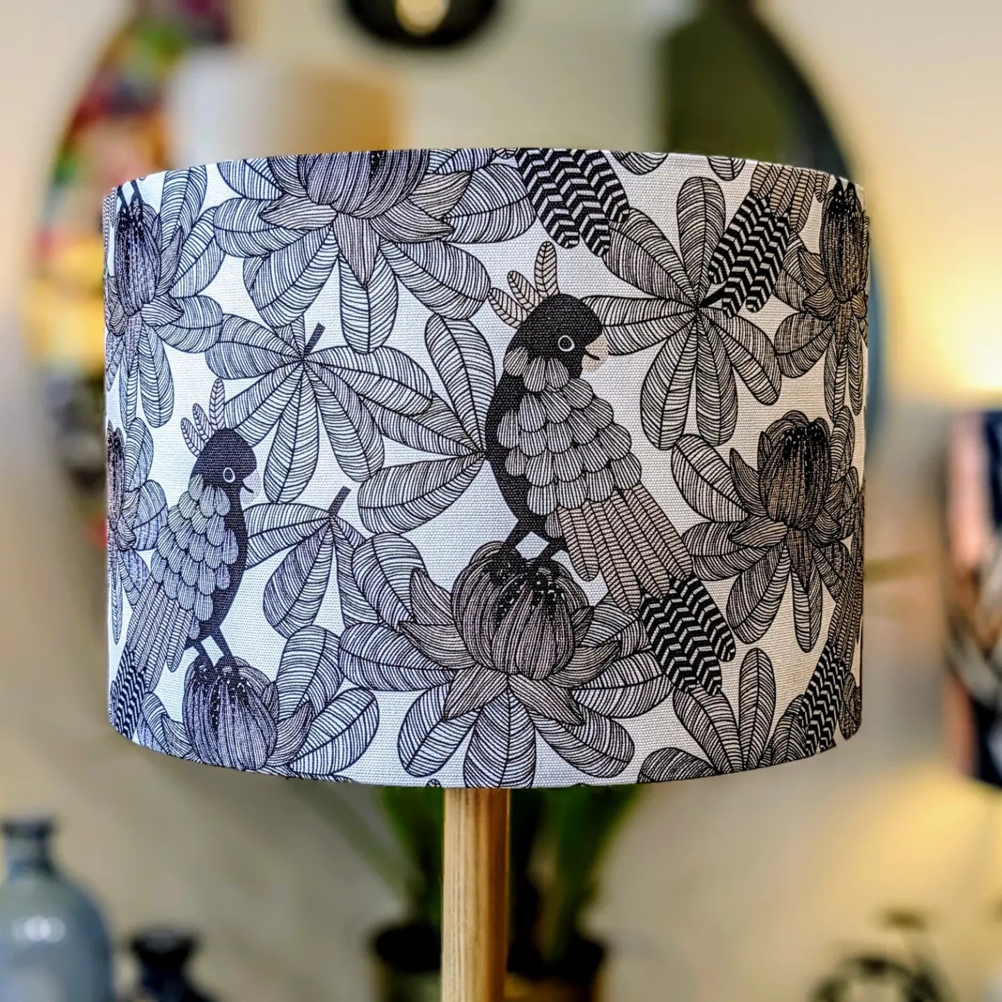 The Australian Cockatoo Lampshade by Emotive Collection features detailed black and white illustrations of birds on branches with large, intricate leaves and flowers, creating a unique handmade piece by an Australian designer.