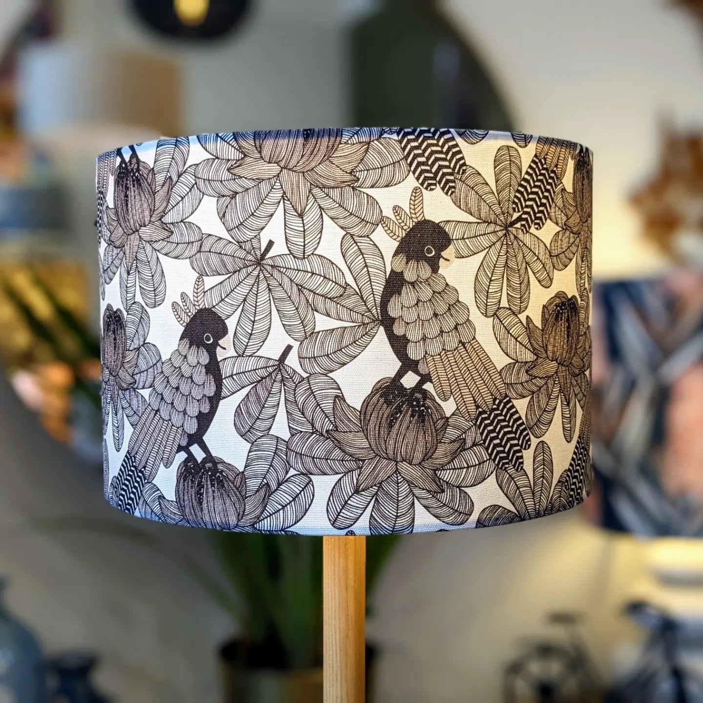 The Australian Cockatoo Lampshade by Emotive Collection features a handmade black and white botanical design of birds among leafy branches and flowers, with a softly blurred background that highlights its intricate abstract patterns.