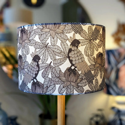 The Australian Cockatoo Lampshade by Emotive Collection features a handmade black and white botanical design of birds among leafy branches and flowers, with a softly blurred background that highlights its intricate abstract patterns.