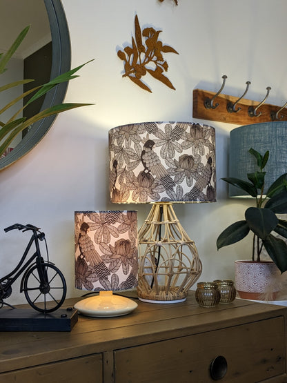 A cozy wooden sideboard displays a decorative bicycle, candle, two Emotive Collection Australian Cockatoo Lampshade lamps, potted plants, and gold candle holders. A mirror, wall hooks, and metal bird wall art hang above.